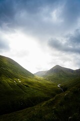 Vertical shot of the Glen Etive in the Scotland highlands with bright sunlight through the clouds - obrazy, fototapety, plakaty