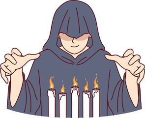 Man monk in hood stands over burning candles, performing mysterious religious ritual
