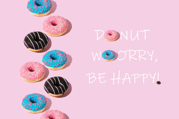 Creative arrangement of colorful donuts on pastel pink background with message "Donut worry, be happy!" Minimal food concept. Trendy yummy donuts idea. Donuts aesthetic background.