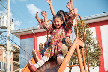 three latin girls playing with their hands up on the slide in an outdoor park - fun concept