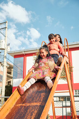 three cheerful latina girls playing on the slide in an outdoor park - friendship concept