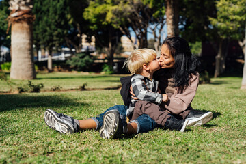 A mother and her three-year-old son sit on the grass in the park