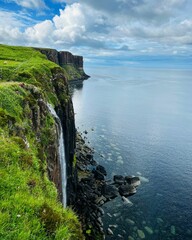 Vertical shot of the Kilt Rocks waterfall flowing down into a sea in the Isle of Skye, Scotland