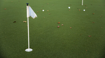 golf ball on the green, poised to sink into the hole, with the flag fluttering in the breeze,...