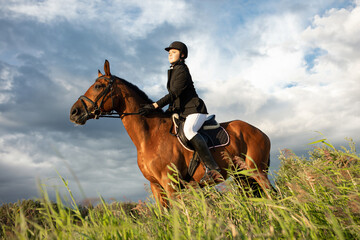 Horsewoman in equestrian sports gear, riding a horse, against an expressive sky, horseback riding in the open air
