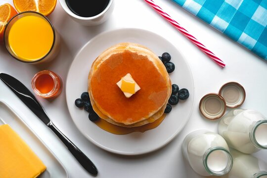 Top view of the pancakes served with butter and honey and a glass of orange juice