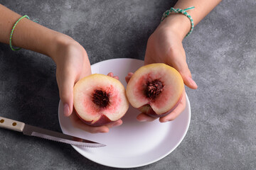 Authentic female hands holding a two half of a fresh ripe peach on white plate on a grey table...