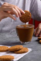Woman's hand dipping a cookie into a transparent cup with coffee with milk in the kitchen, have...
