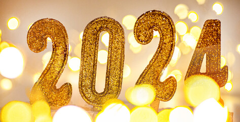 2024 New Year Background. Text by candles with christmas lights and bokeh on gold background.