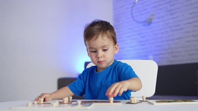 Adorable little toddler in blue t-shirt playing peacefully at the desk. Baby boy matching puzzle pieces. Blurred backdrop.