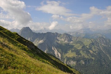 Obraz premium Mesmerizing shot of a steep slope of a grass mountain with montane forests in the background