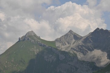 Scenic view of the rocky peaks of green mountains under cloudy sky on a sunny day