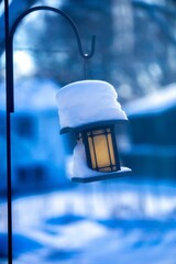 Vertical shot of a street lantern outdoors covered in a big layer of snow in blurred background