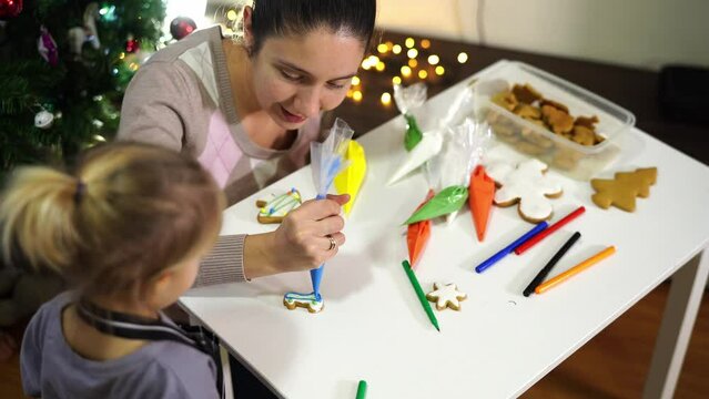 Little girl looks at her mother painting cookies with cream from a pastry bag