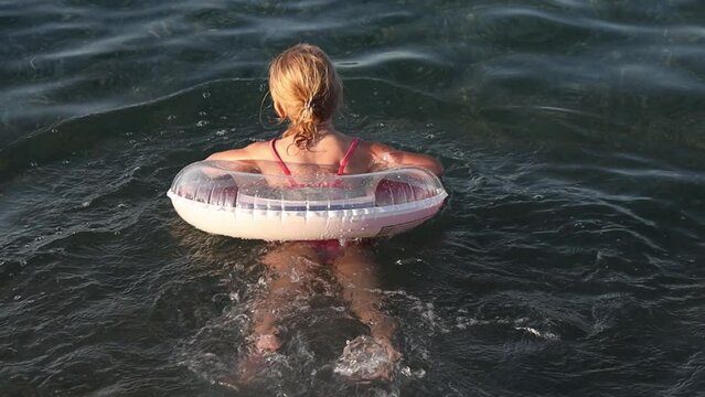 Little girl swims with an inflatable ring in the sea.