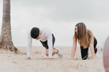 Young athletic couple working out on the beach in a planking position