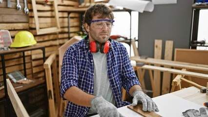 Young blond man, a relaxed carpenter, closes his eyes and strikes a yoga meditation gesture in his carpentry studio. embracing the zen lifestyle at the workplace.