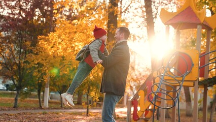 Young father extends arms to lift little daughter during walk in autumn park