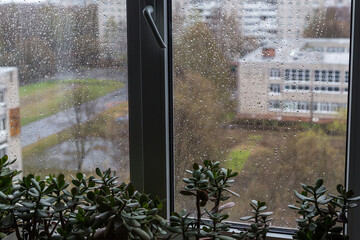 Rain drops on window glass close up background texture. View on defocused street, town from house,...