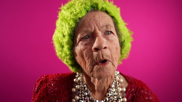 Smiling happy fisheye view of successful funny elderly woman with no teeth and green hat isolated on pink background. Caricature of peoples emotions