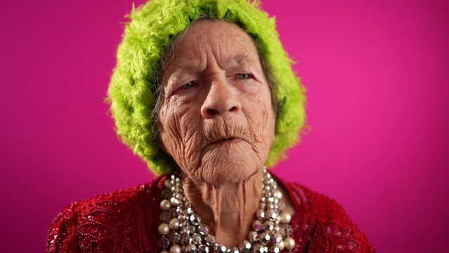 Smiling happy fisheye view of successful funny elderly woman with no teeth and green wig or hat isolated on pink background in slow motion. Caricature of peoples emotions
