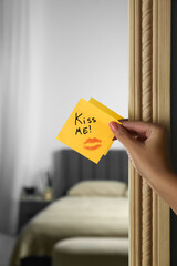 Woman attaching sticky note with phrase Kiss Me to mirror in room