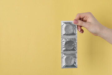 Woman holding condoms on pale yellow background, closeup. Space for text