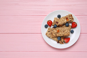 Tasty granola bars and berries on pink wooden table, top view. Space for text