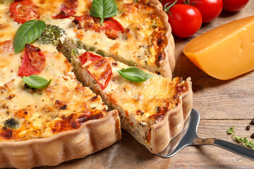 Taking piece of tasty quiche with tomatoes, basil and cheese on wooden table, closeup