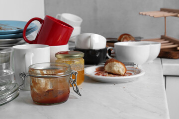 Many dirty utensils, dishware and food leftovers on countertop in messy kitchen
