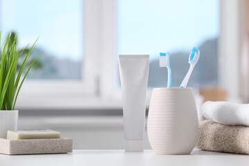 Plastic toothbrushes in holder, toothpaste, soap bar and towels on white table indoors