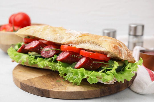 Delicious sandwich with sausages and vegetables on white table, closeup