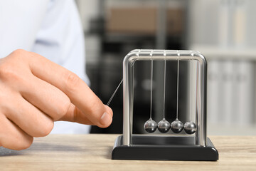 Man playing with Newton's cradle at wooden table, closeup. Physics law of energy conservation - obrazy, fototapety, plakaty