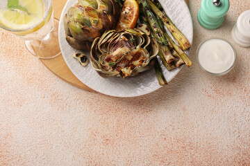 Tasty grilled artichokes and asparagus served on beige textured table, flat lay. Space for text