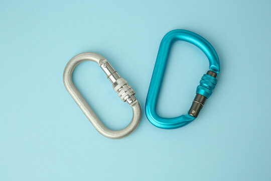 Two metal carabiners on light blue background, flat lay