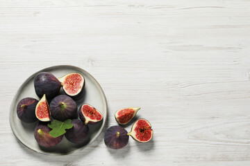 Whole and cut ripe figs with leaf on white wooden table, flat lay. Space for text