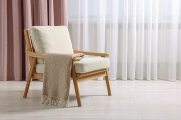 Comfortable armchair with blanket in room, space for text