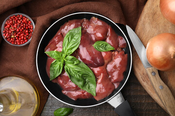 Raw chicken liver with basil in frying pan and products on wooden table, flat lay - obrazy, fototapety, plakaty