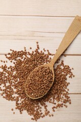 Spoon with dry buckwheat on light wooden table, top view