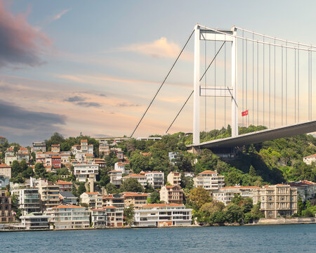 View from the sea of the European side of Bosphorus strait, Istanbul, Turkey, with traditional waterfront houses, under Bosphorus bridge, and green hill with dense trees, in a summer day after sunrise