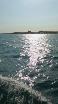 Serene slow-motion captures the island of Rua in the Arousa estuary, as a boat glides through radiant summer seas. Sunlight dances on the tranquil waves, painting a vivid scene of coastal bliss.