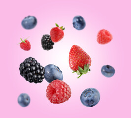 Fresh ripe blueberries, strawberries, raspberries and blackberries falling on pink background