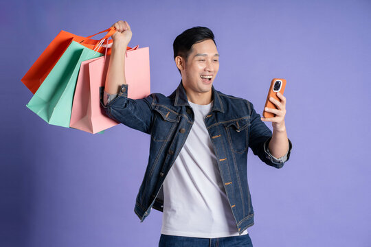 Image of asian man using phone and shopping bag on purple background