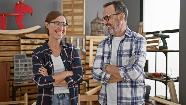 Two confident carpenters, man and woman, beaming as they stand together with arms crossed in professional woodwork business, symbol of partnership and expertise in carpentry industry
