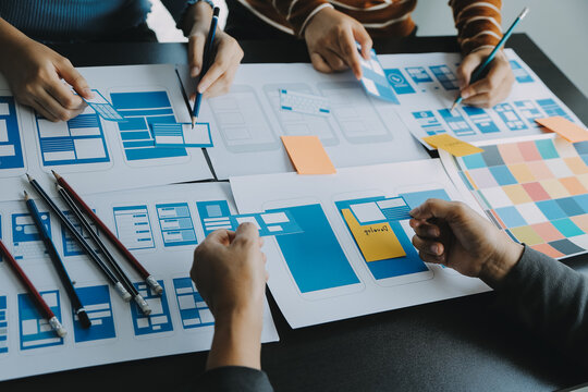 Close up ux developer and ui designer brainstorming about mobile app interface wireframe design on table with customer breif and color code at modern office.Creative digital development agency