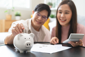 Happy asian family young couple love hand holding piggy bank to save and model house for saving money wealth to buy real estate for new home. Financial planning, business finance concept. Housing loan - obrazy, fototapety, plakaty