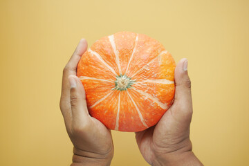hand holding Pumpkin on orange color background 