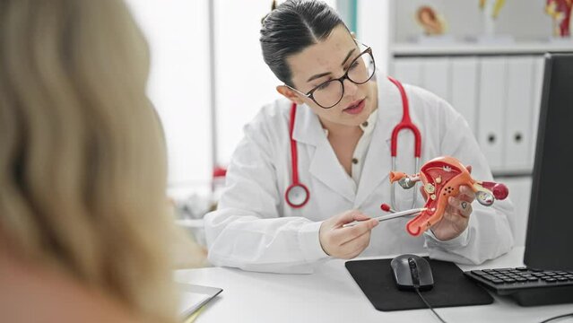 Young beautiful hispanic woman doctor showing female reproductive system at the clinic