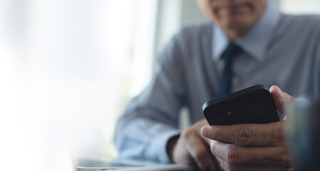Fototapeta premium Close up of businessman using mobile smart phone during working on laptop computer at office. Asian business man hand holding smartphone, connecting the internet, online working