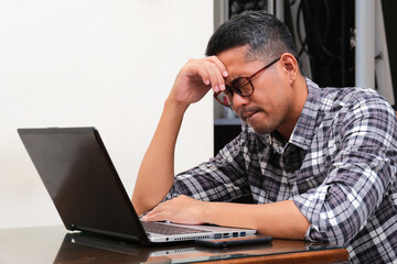 Adult Asian man sitting in front of laptop with stress expression